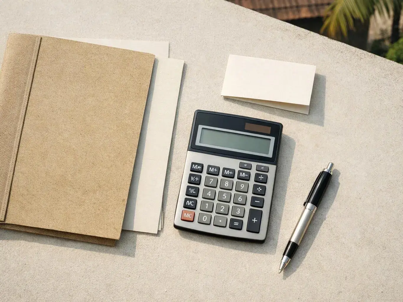 A notebook, blank cards, calculator, and pen sit neatly on a sunlit desk